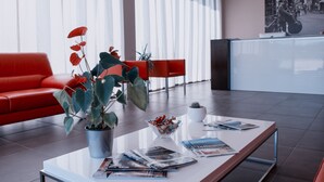 Un hall moderno con un sofá rojo, una mesa de centro con revistas, una planta en maceta y una recepción.