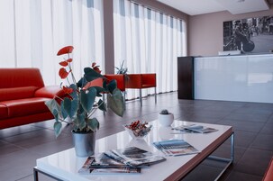 A modern lobby with a red sofa, a coffee table with magazines, a potted plant, and a reception desk.