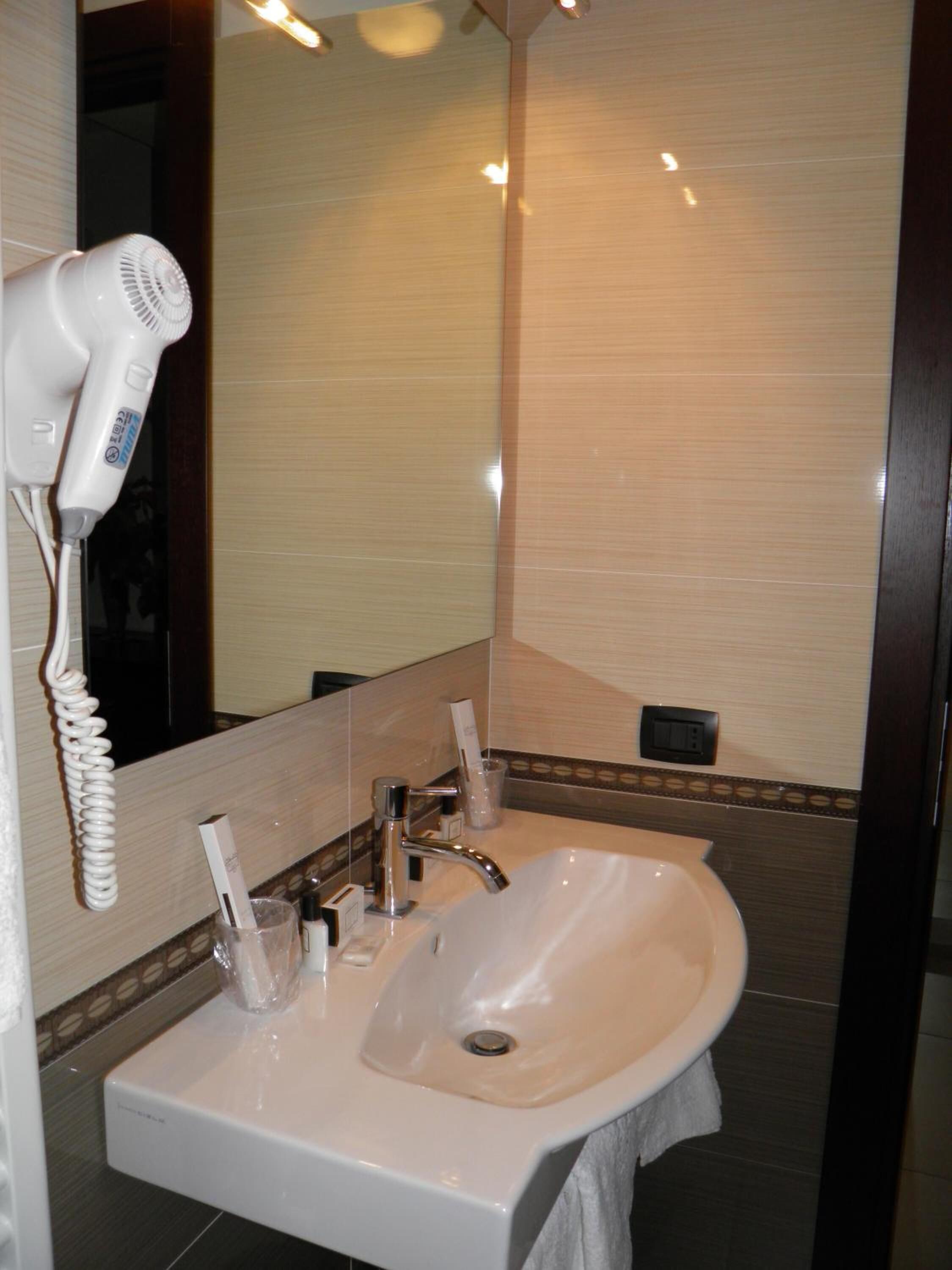 Un baño con lavamanos blanco, un secador de pelo y un espejo.