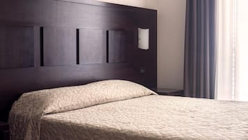 Ein Hotelzimmer mit dunkelholzvertäfelter Kopfteile, einer beigen Bettdecke mit Muster und einer weißen Wandleuchte.