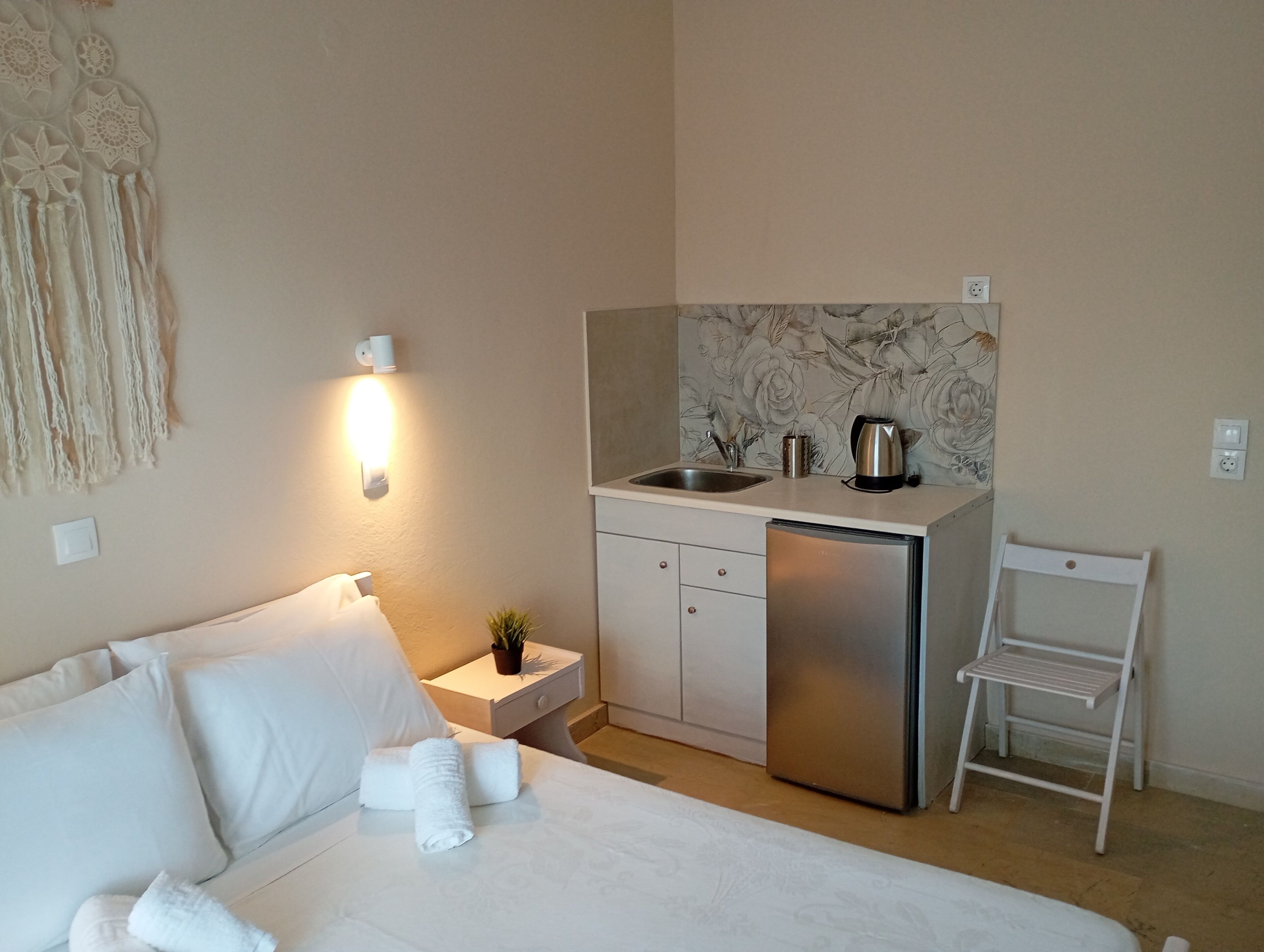 Une chambre d’hôtel de taille réduite, comprenant un lit, une petite kitchenette, une table de chevet avec une lampe et un luminaire fixé au mur.