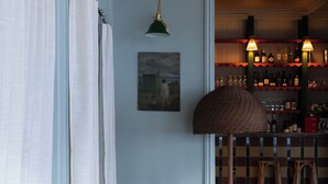 A room with a dining table, chairs, a lamp, and a bar area with shelves. - Marnie House Hôtel (Le Touquet-Paris-Plage)