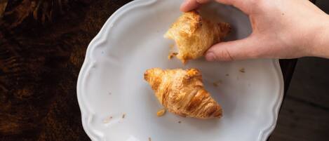 A wooden table with a white plate holding two croissants and a cup of coffee.