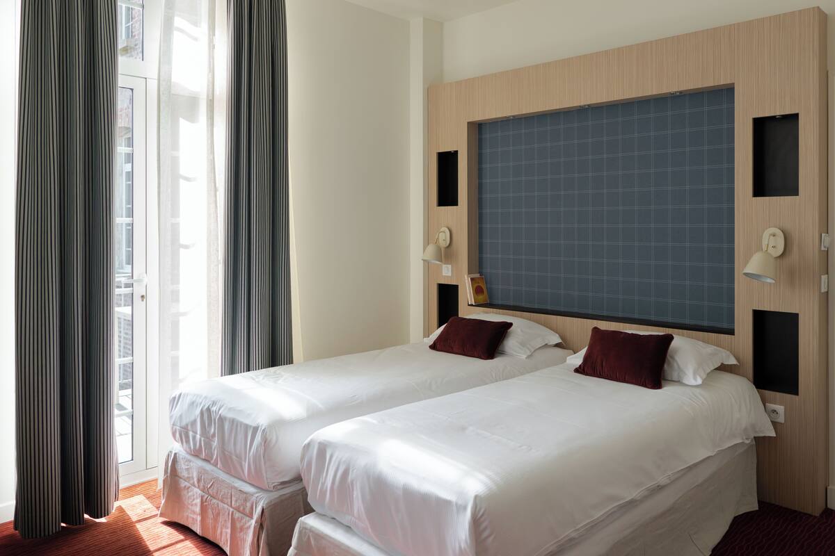 A hotel room with two beds, a large window, and a view of the city.