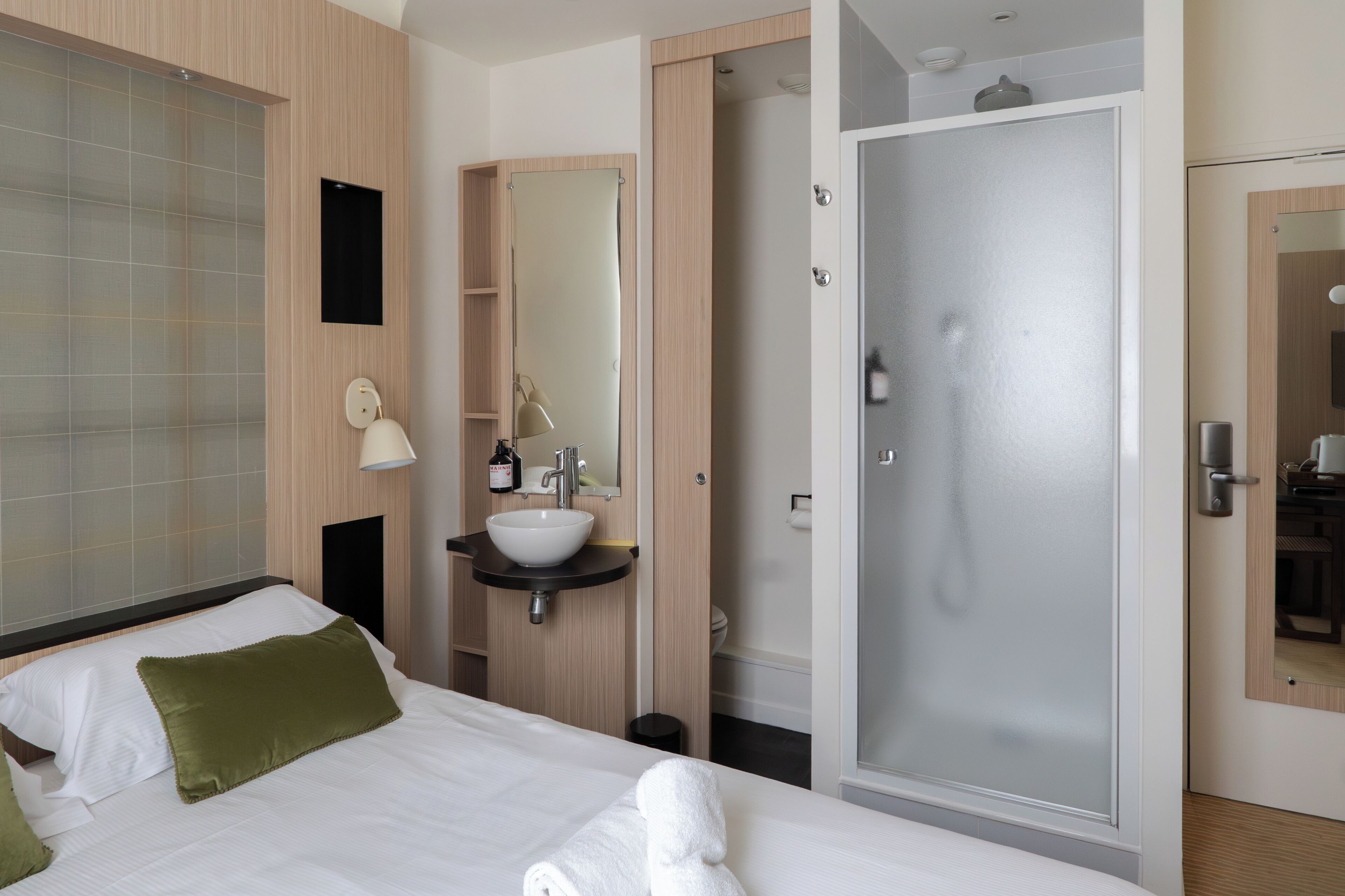 Une chambre d’hôtel avec un lit, une salle de bain comprenant un lavabo, un miroir et une douche.