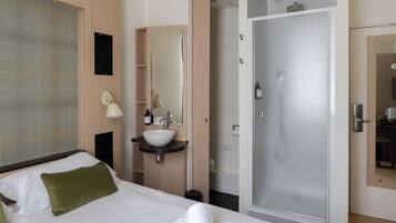 Une chambre d’hôtel avec un lit, une salle de bain comprenant un lavabo, un miroir et une douche.