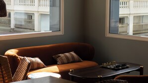 A room with a sofa, a table, and chairs, a window with a view of buildings, and a lamp. - Marnie House Hôtel (Le Touquet-Paris-Plage)