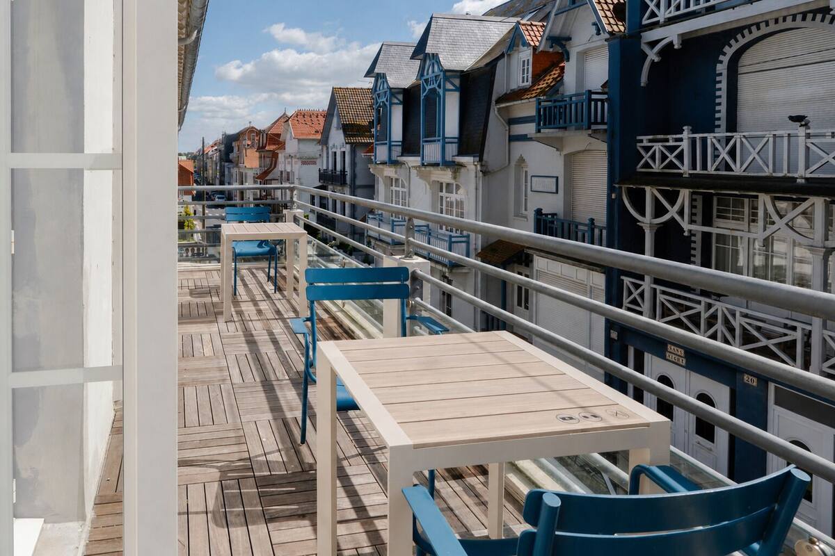 A balcony with wooden flooring, blue chairs, and a table.