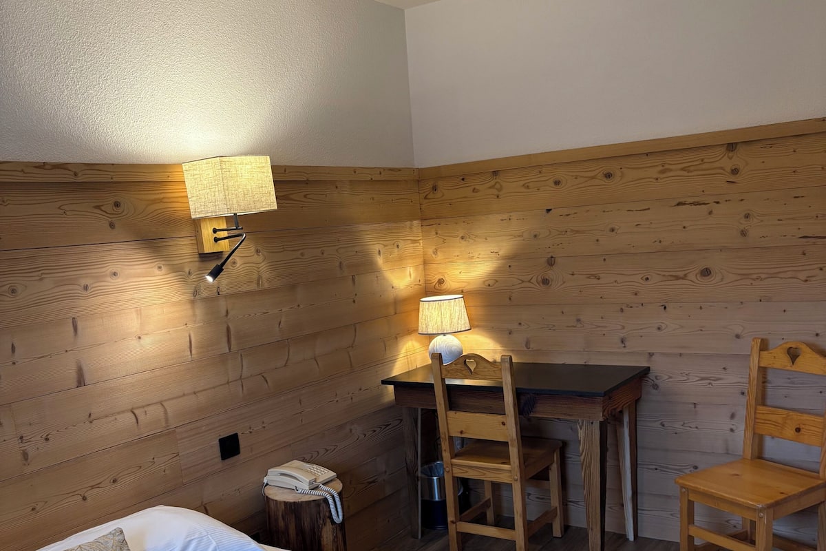 Un dormitorio con una cama, una mesita de noche, una lámpara, una mesa de madera y dos sillas.