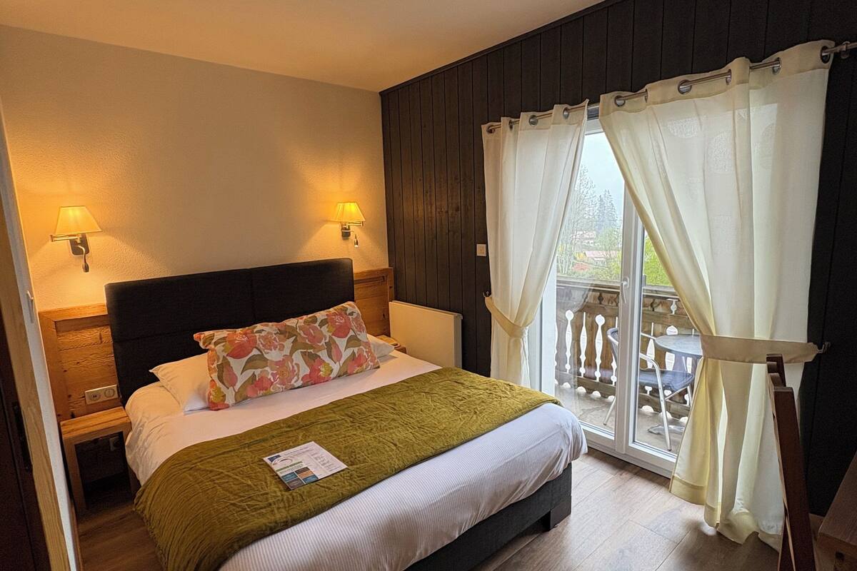 Un dormitorio con cama, dos lámparas de noche, ventana con cortinas y vistas al exterior.