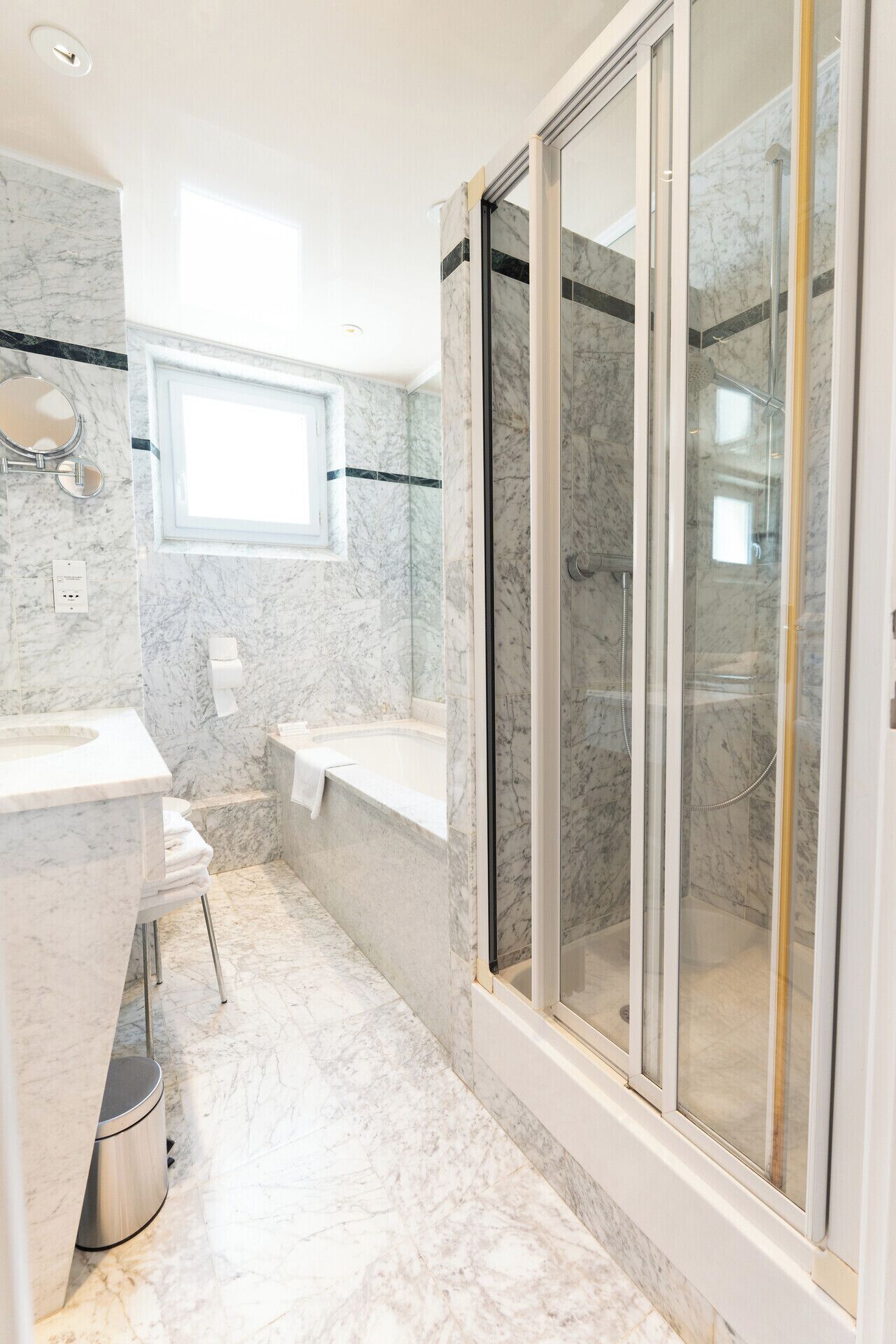 Ein Badezimmer mit Marmorboden, einer Badewanne, einer Duschkabine und einem Waschtisch mit Spiegel.