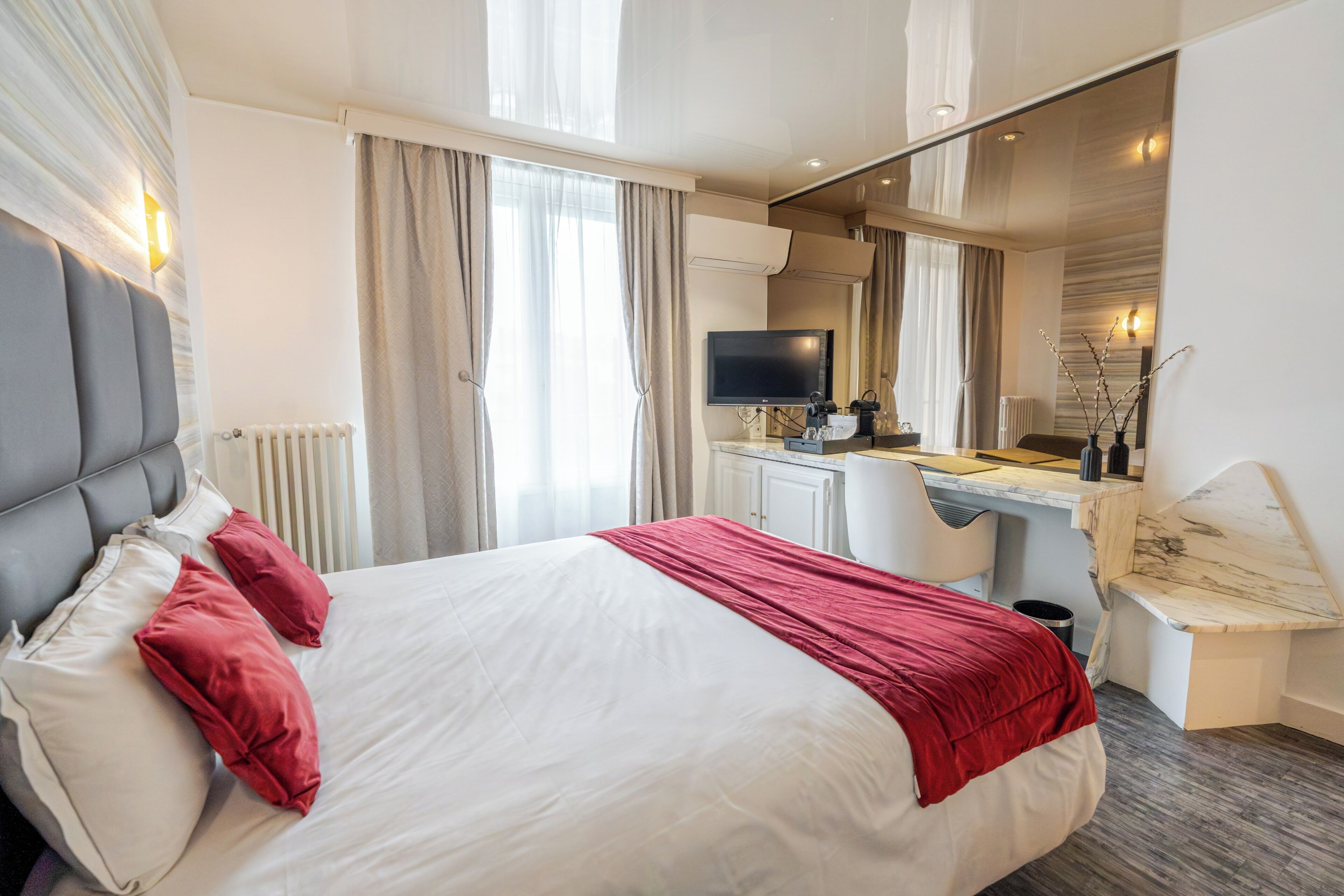 Una habitación de hotel con cama, escritorio, televisión y espejo.