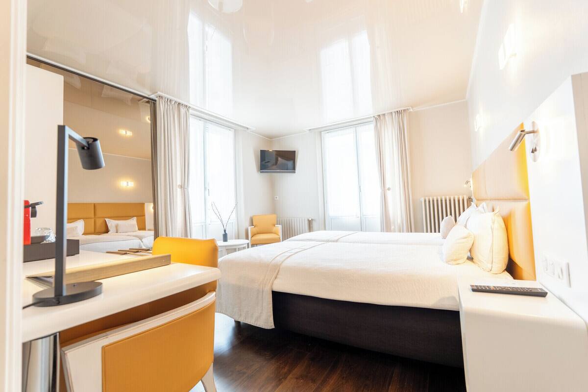 Una habitación de hotel moderna con una cama grande, un escritorio con lámpara, una silla y un televisor montado en la pared.