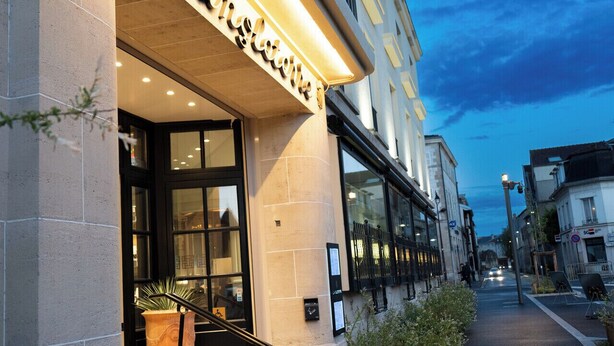 A hotel entrance with a modern facade, large windows, and a visible staircase leading to the entrance.