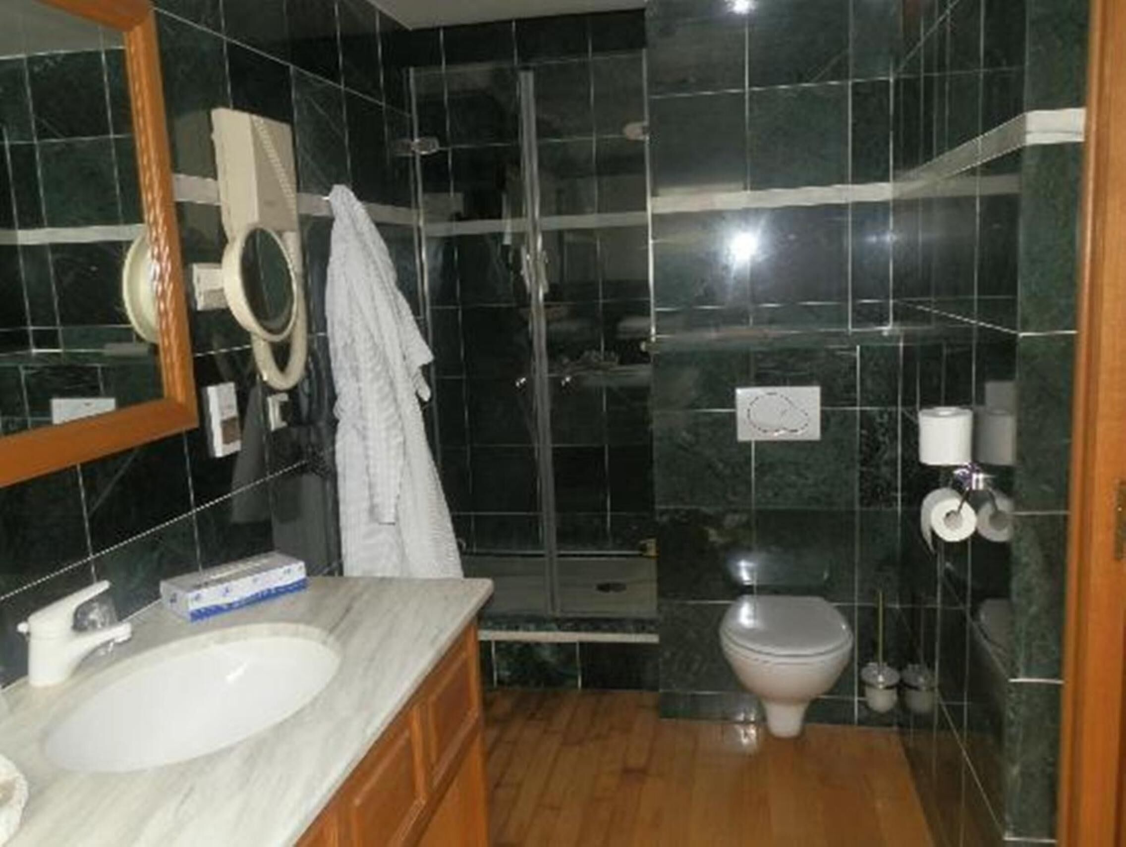 Un baño con lavamanos de mármol, inodoro, cabina de ducha de vidrio y espejo con una toalla colgada.