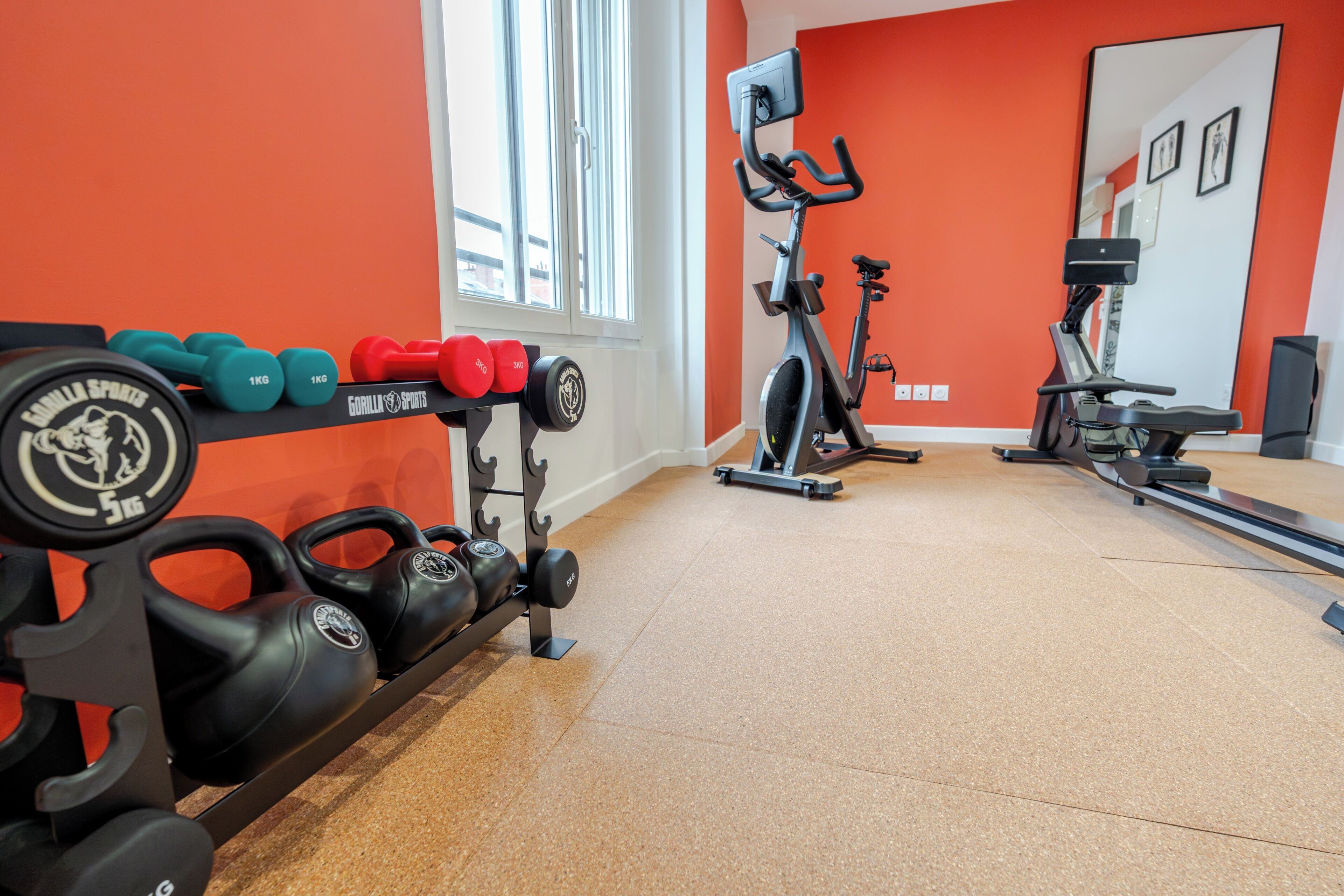 A gym with weightlifting equipment, cardio machines, and a bright orange wall.