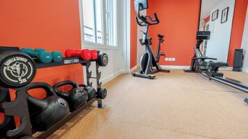 A gym with weightlifting equipment, cardio machines, and a bright orange wall.