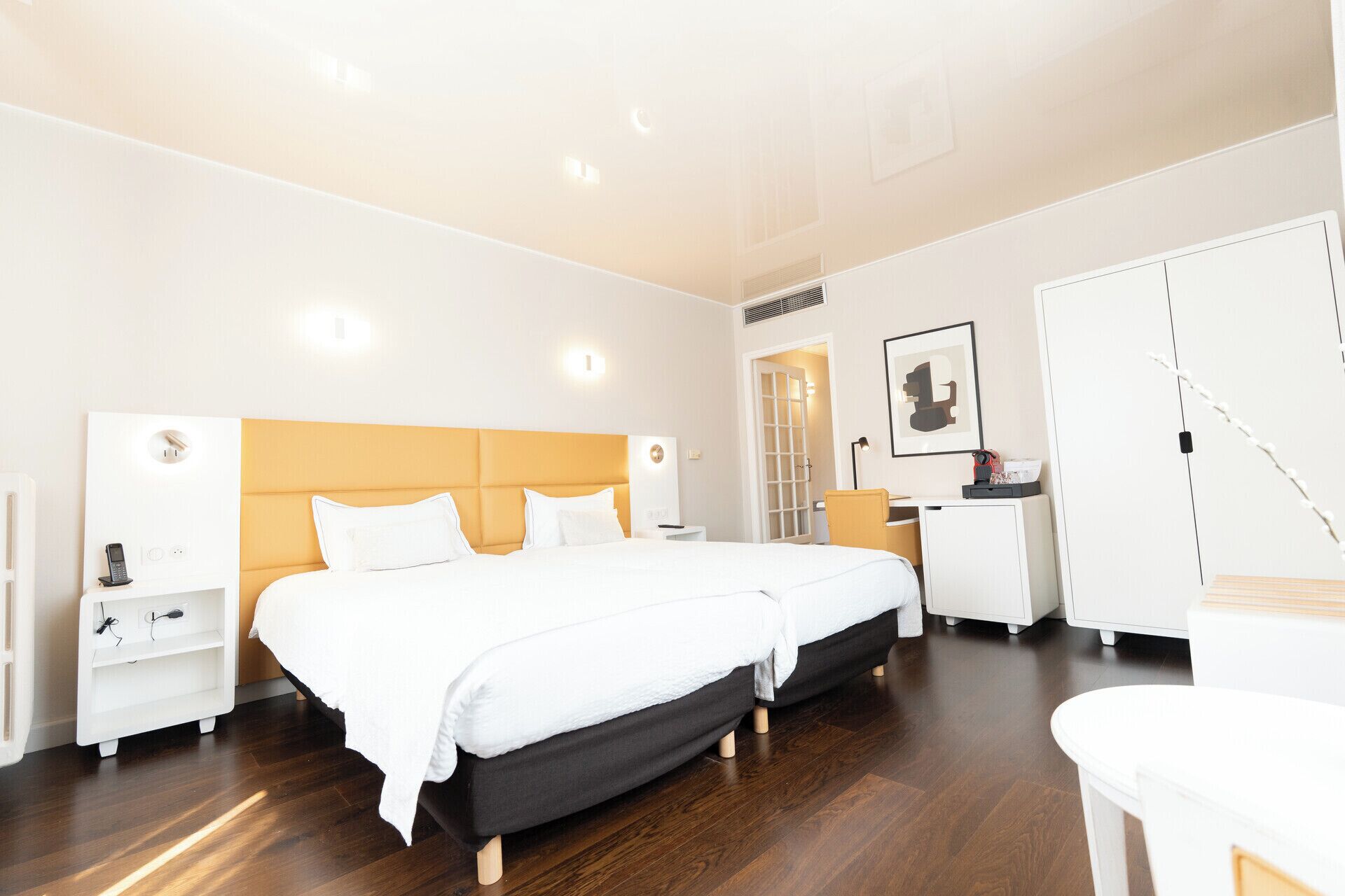 A hotel room with two beds, a desk, a wardrobe, and a bathroom.