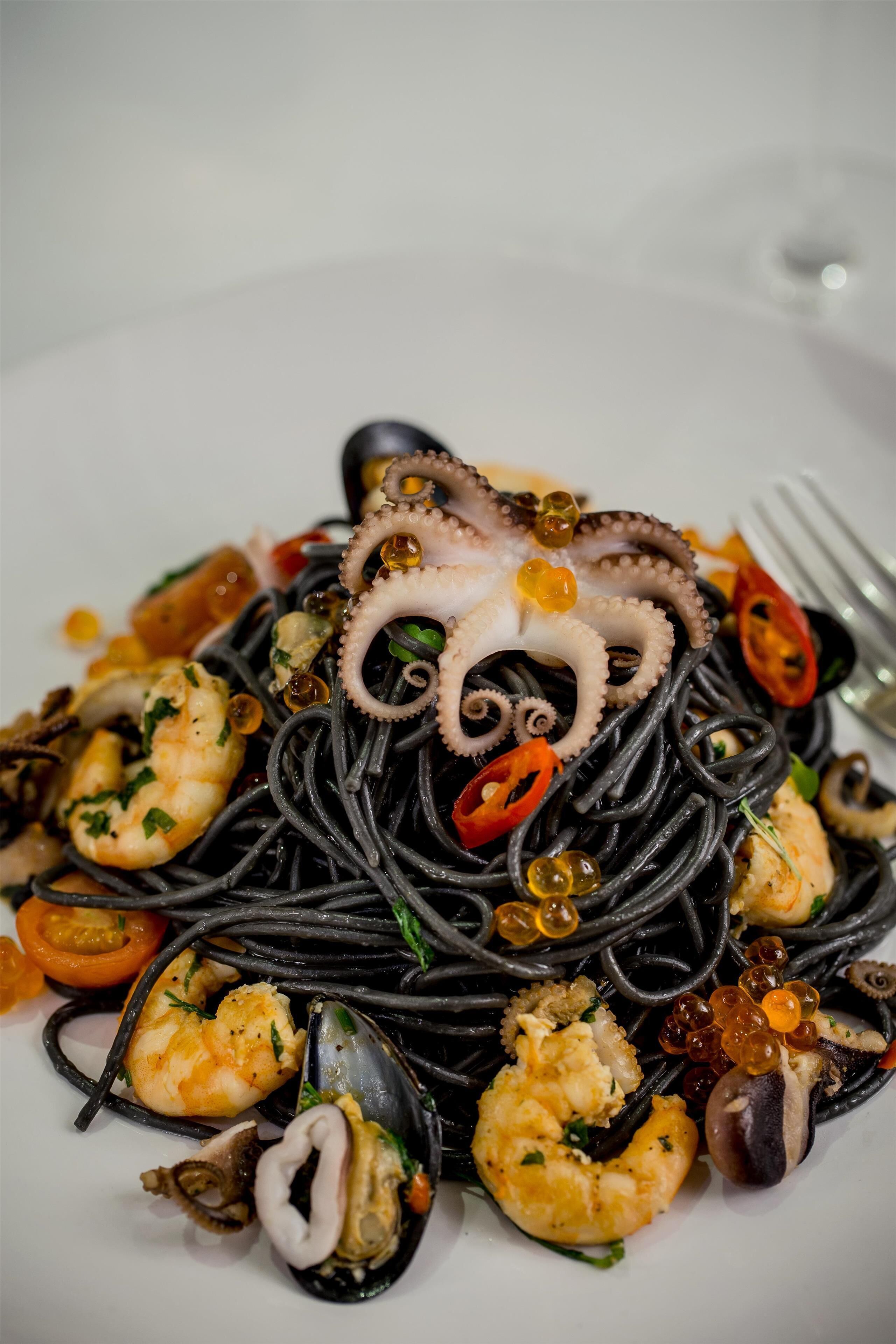 A plate of black pasta with seafood, including shrimp and mussels, garnished with herbs and chili slices.