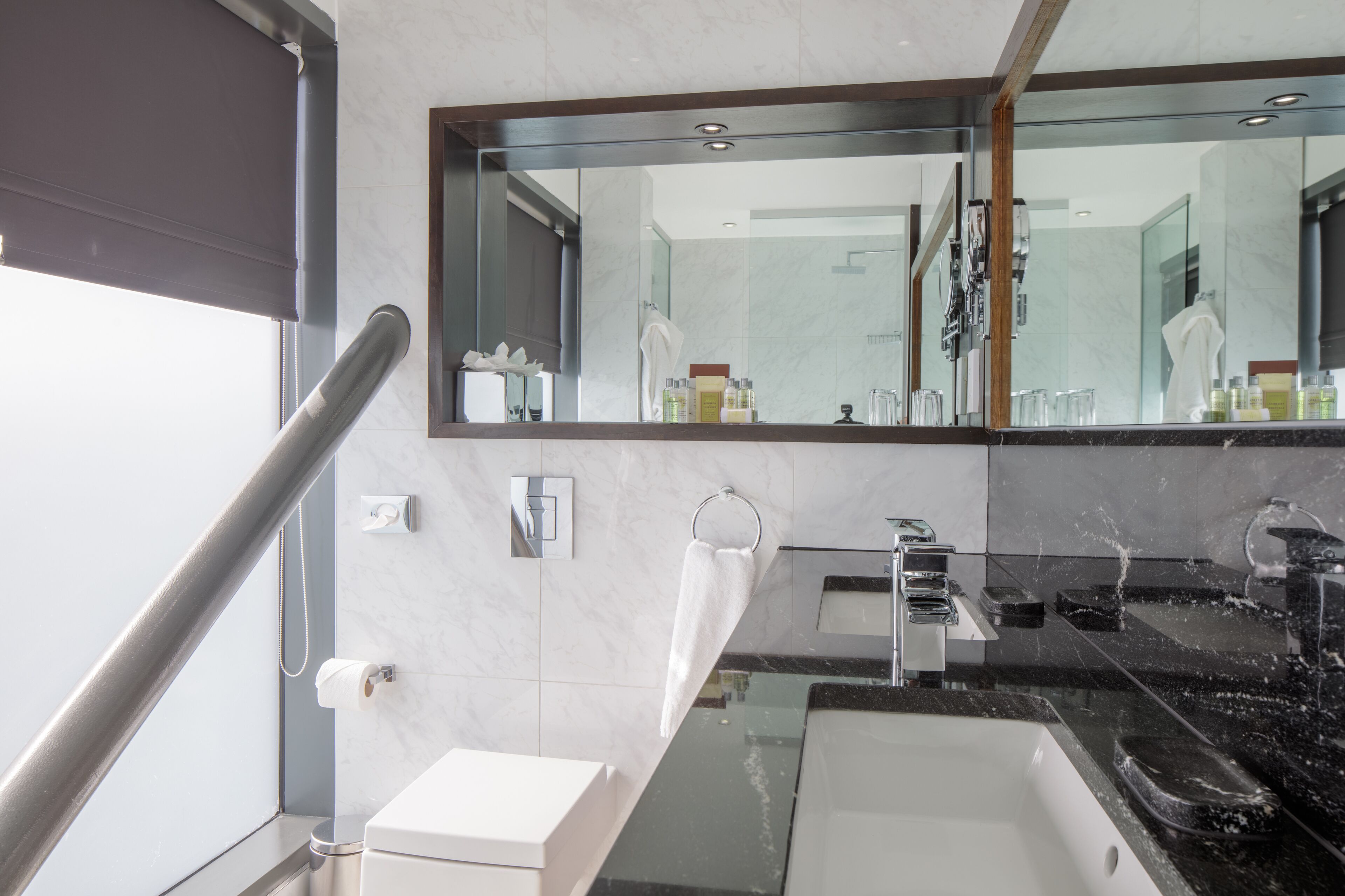 A modern bathroom with a large mirror, two sinks, and a glass shower enclosure.