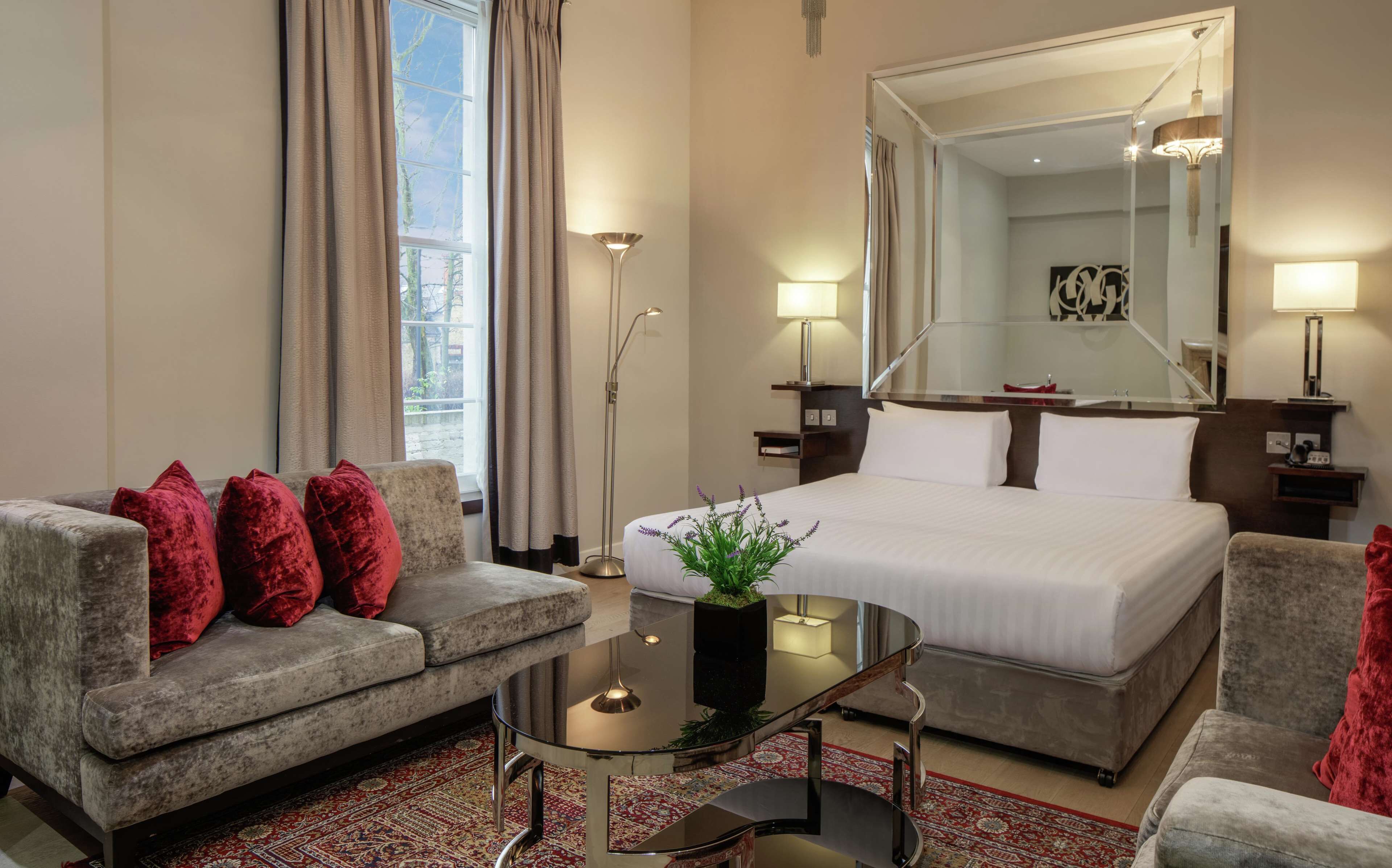 A hotel room with a bed, a sofa, a coffee table, a floor lamp, and a large mirror.