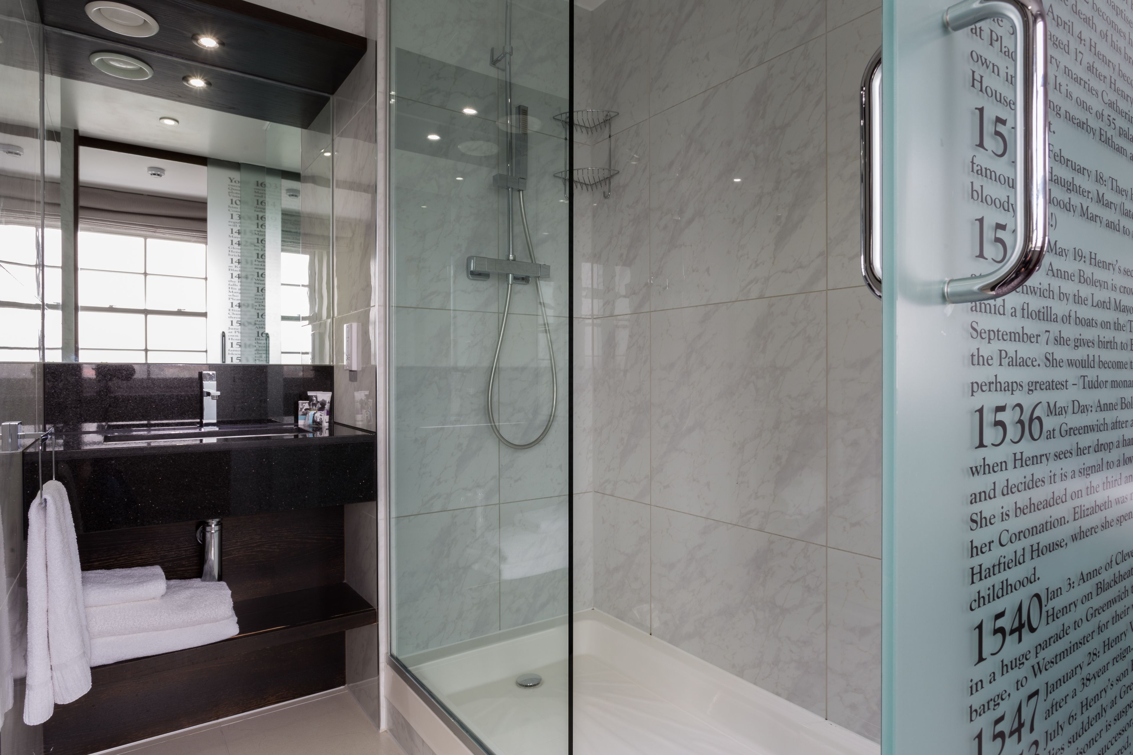 A modern bathroom with a glass shower enclosure, a dark vanity, and a large mirror.
