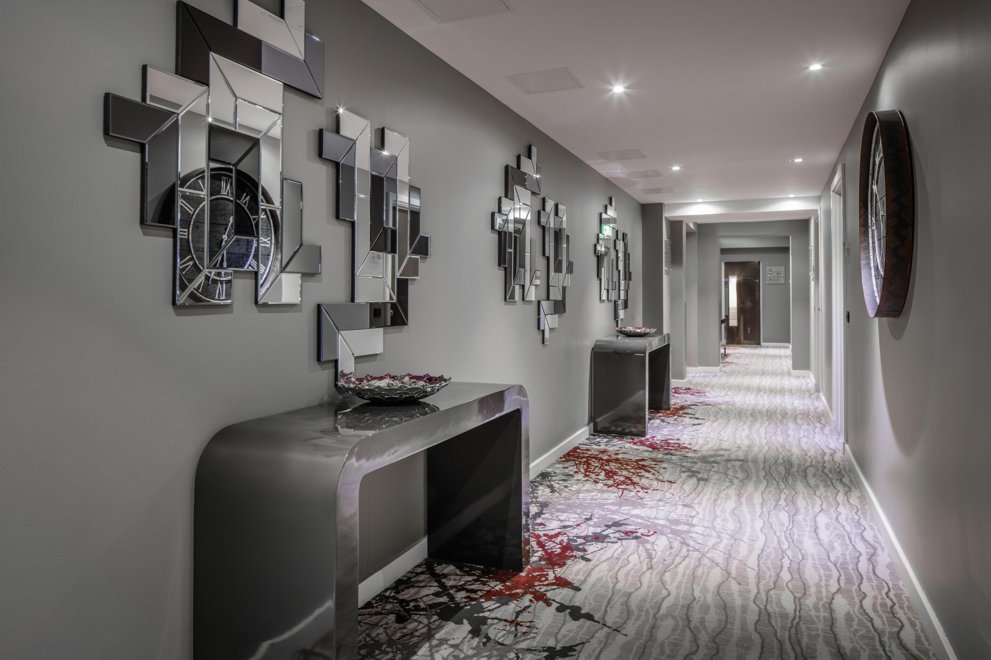 A modern hallway with a patterned carpet, a reflective wall clock, and a console table with a decorative bowl.