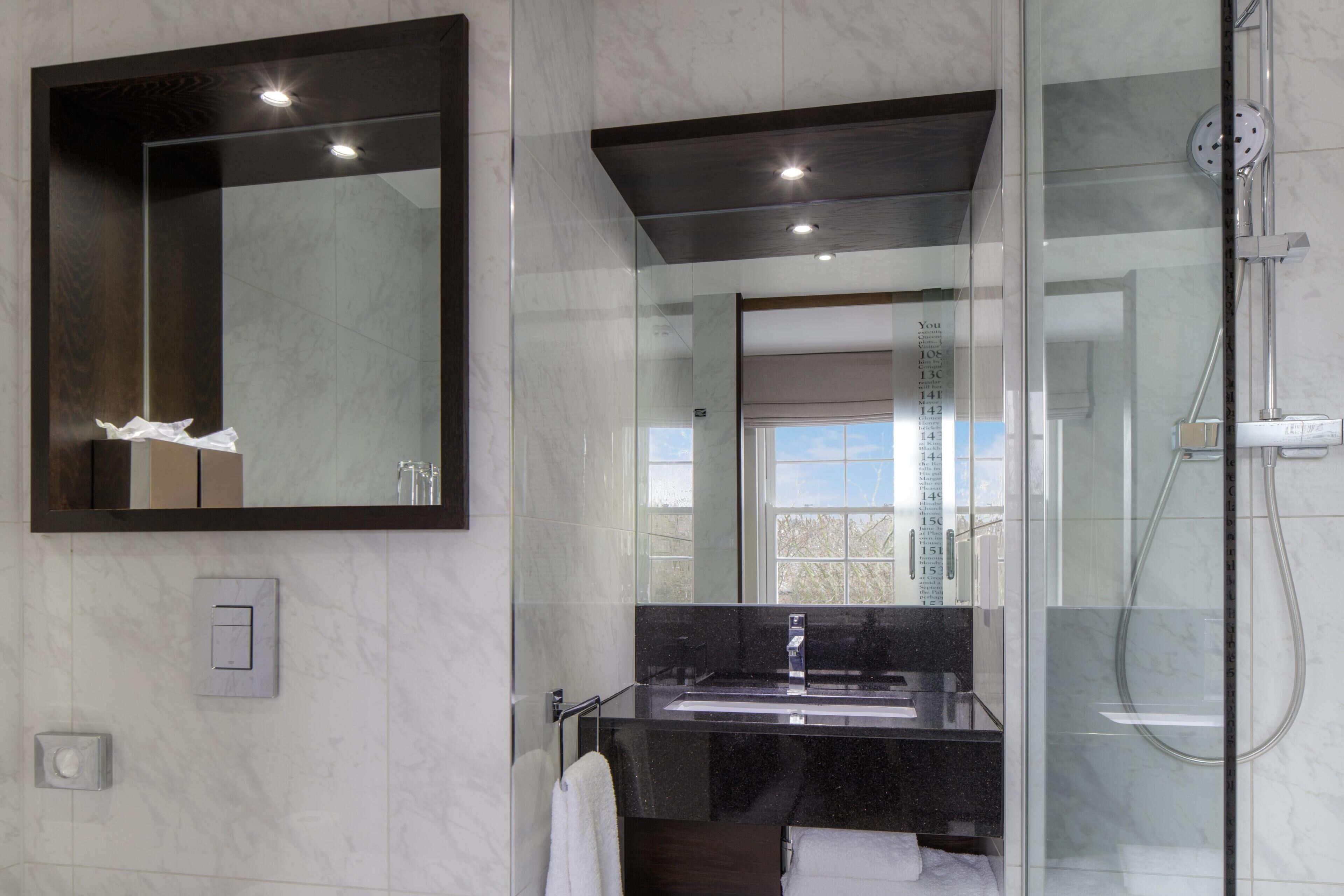 A modern bathroom with a large mirror, a glass shower enclosure, and a marble-tiled wall.