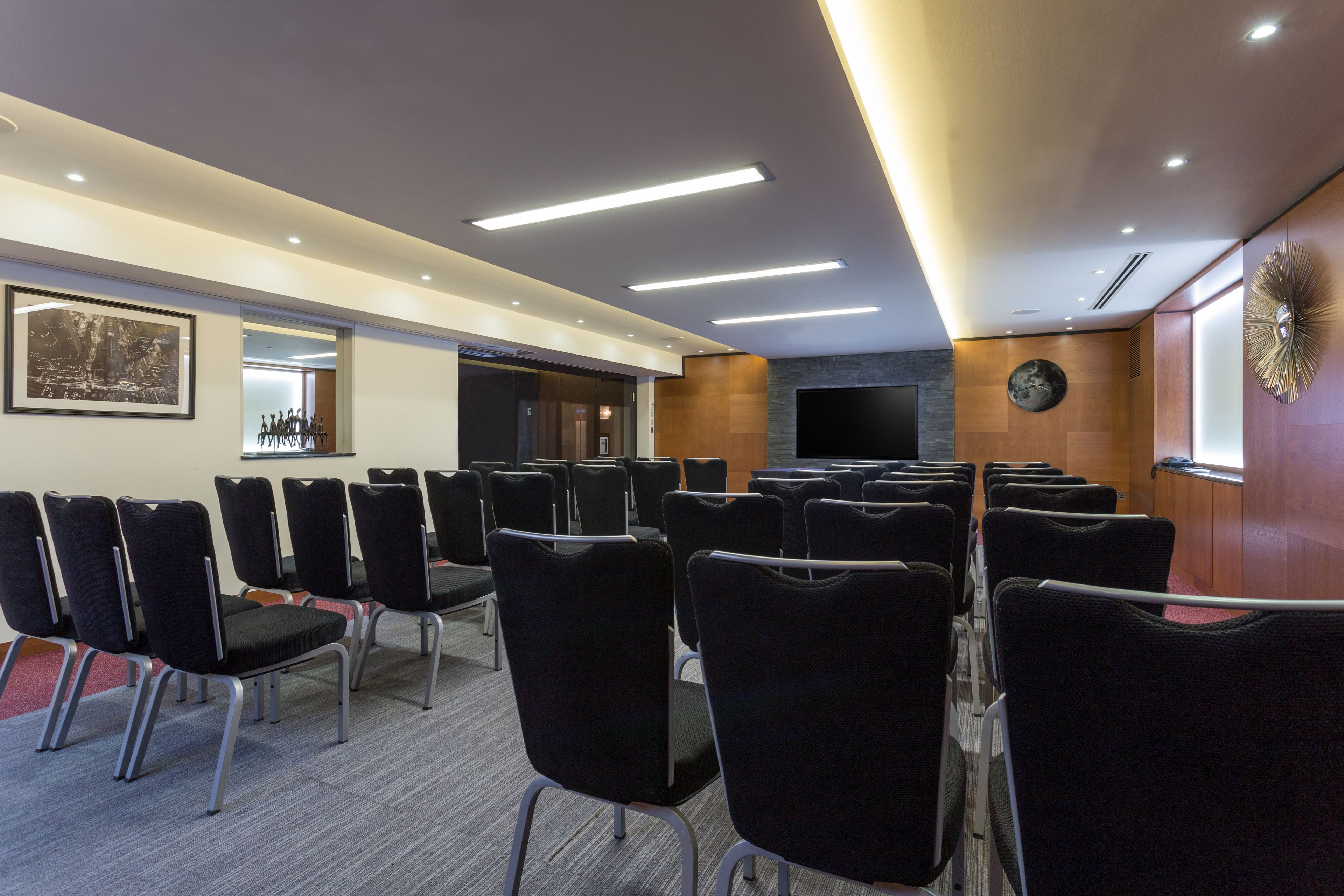A conference room with rows of black chairs, a large framed picture on the wall, and a round decorative item on the wall.