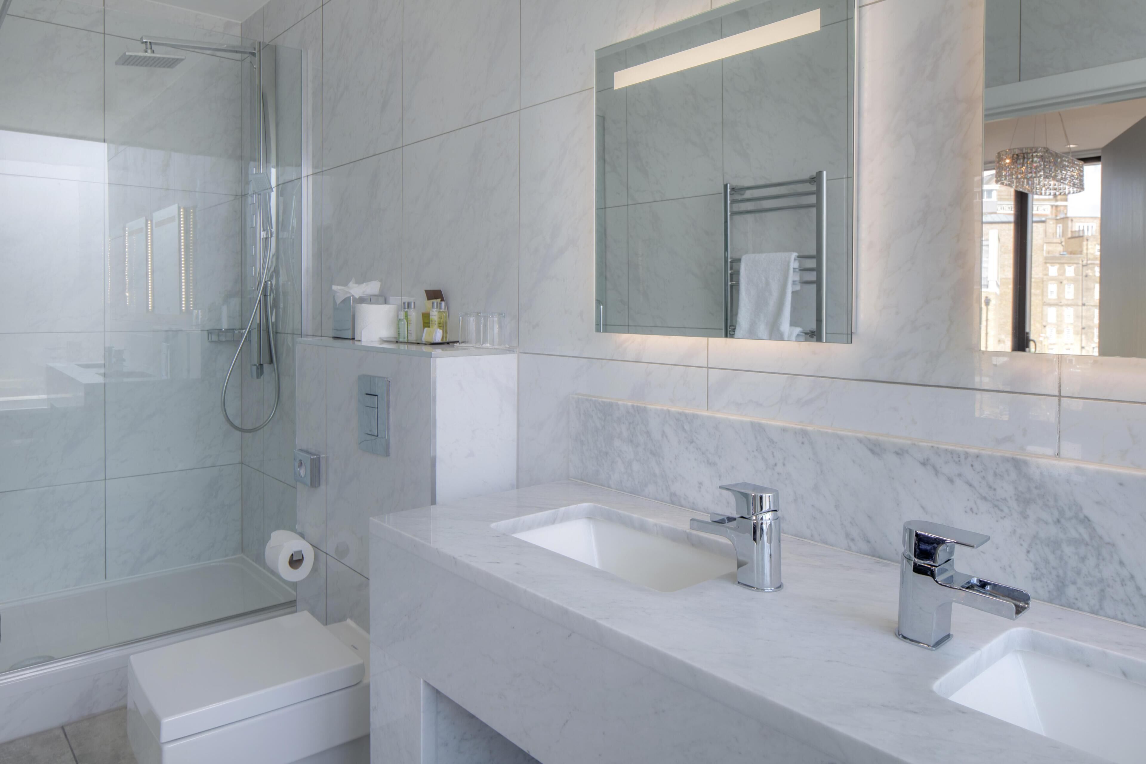 A modern bathroom with a glass shower enclosure, two sinks with chrome faucets, and a large mirror above the vanity.