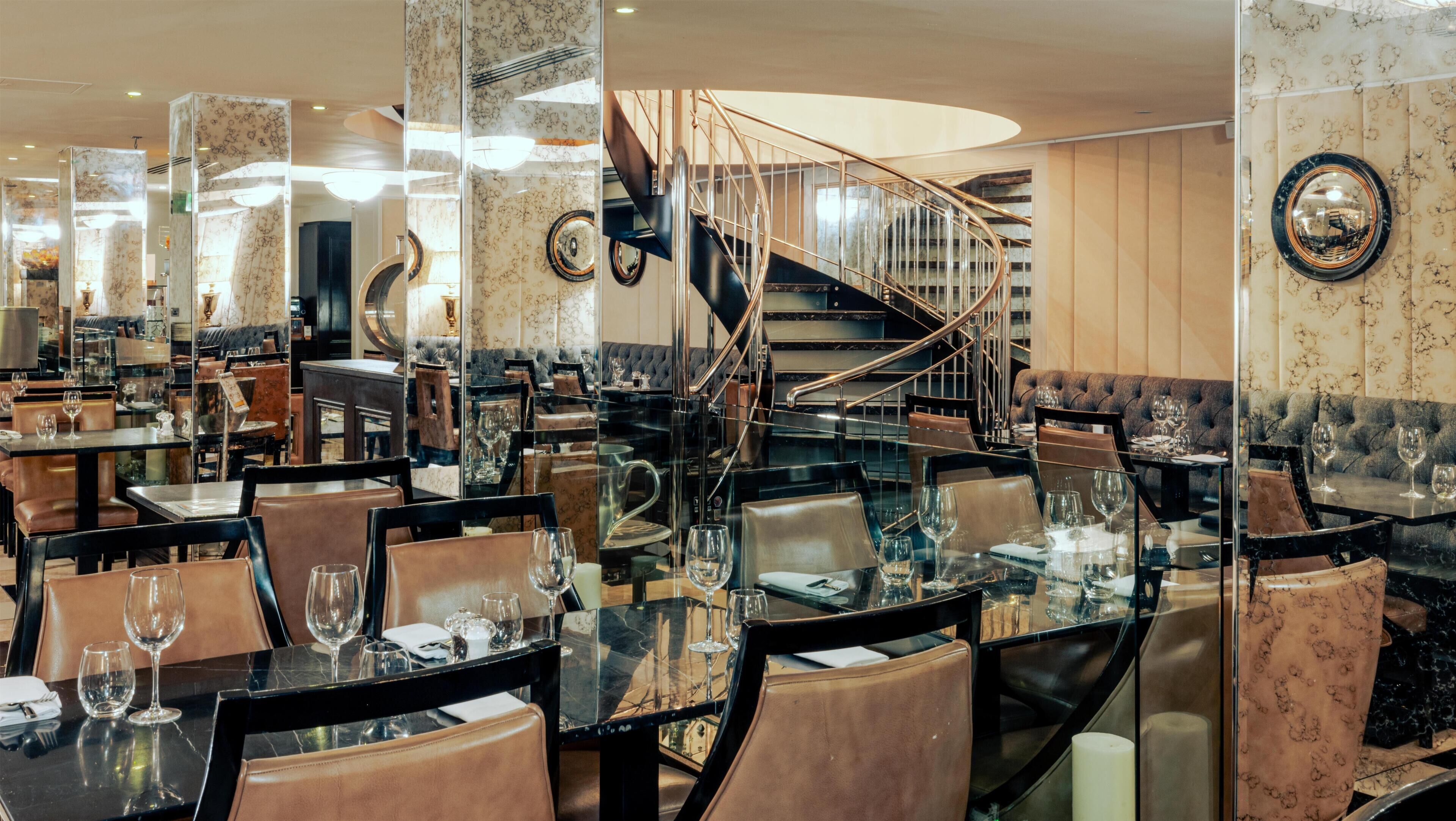 Un restaurant avec des tables et des chaises en verre, un escalier en colimaçon et un coin bar.