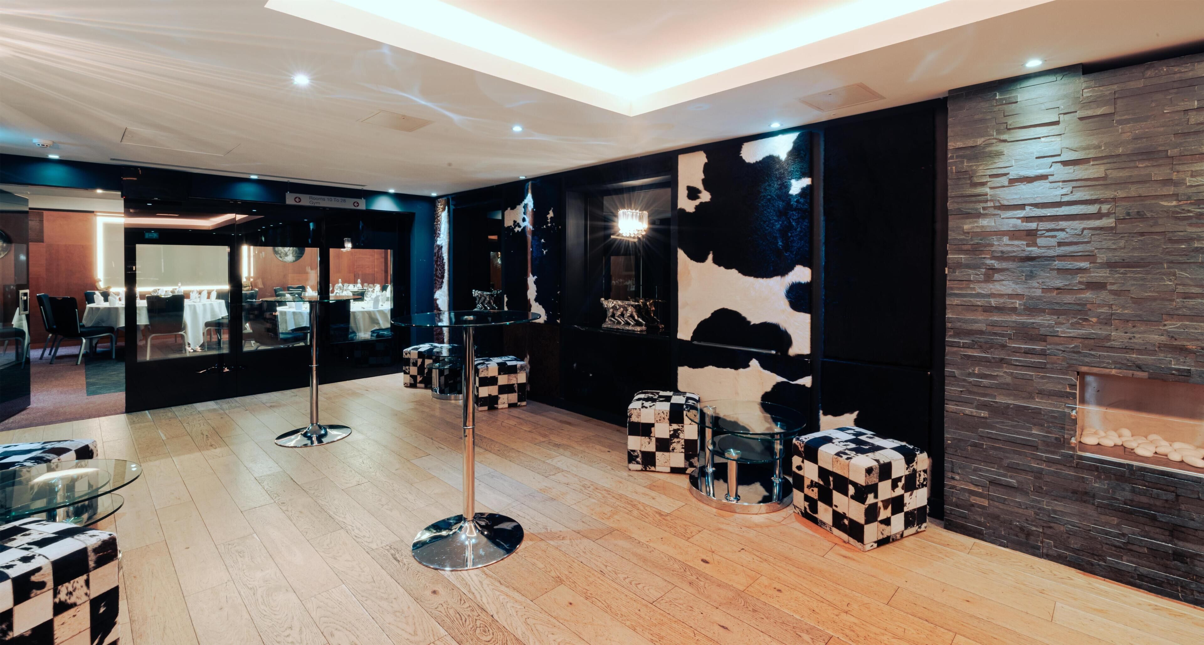 A modern interior with a central glass table, checkered stools, and a stone wall with a cow print design.