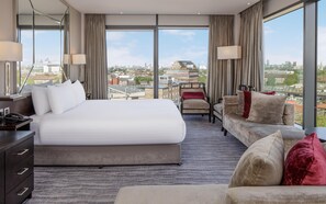 A hotel room with a large bed, a sofa, a desk with a phone, and a view of the cityscape.
