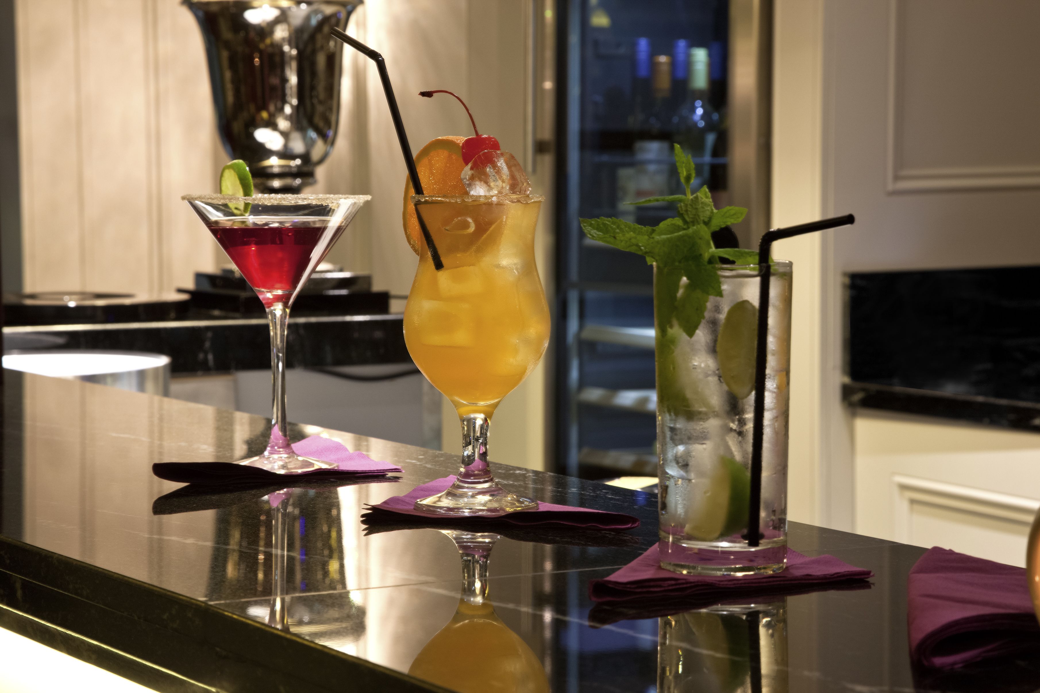 Three cocktails on a bar counter with a reflective surface.
