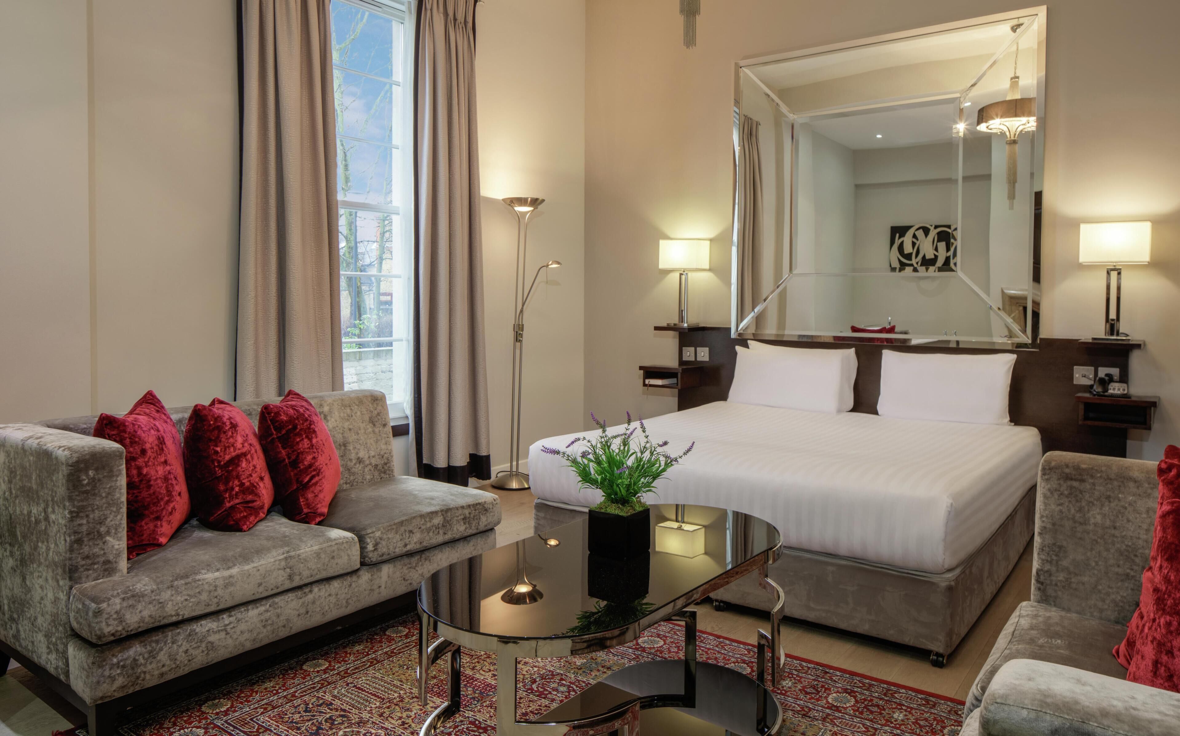 Een hotelkamer met een bed, een bank, een salontafel, een vloerlamp en een grote spiegel.