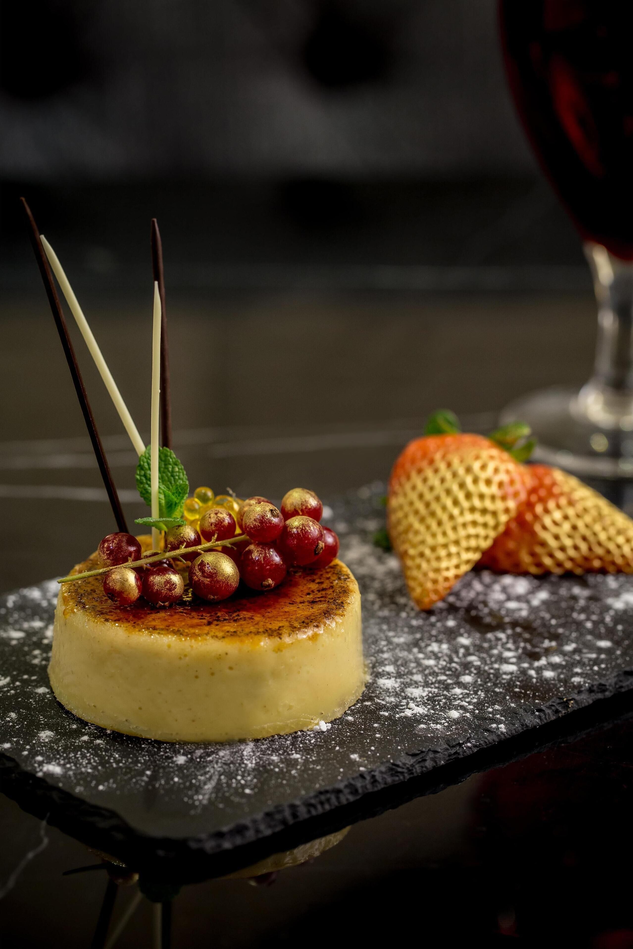Un dessert su un piatto in ardesia nera, spolverato di zucchero a velo e guarnito con uva rossa, menta e una fragola.