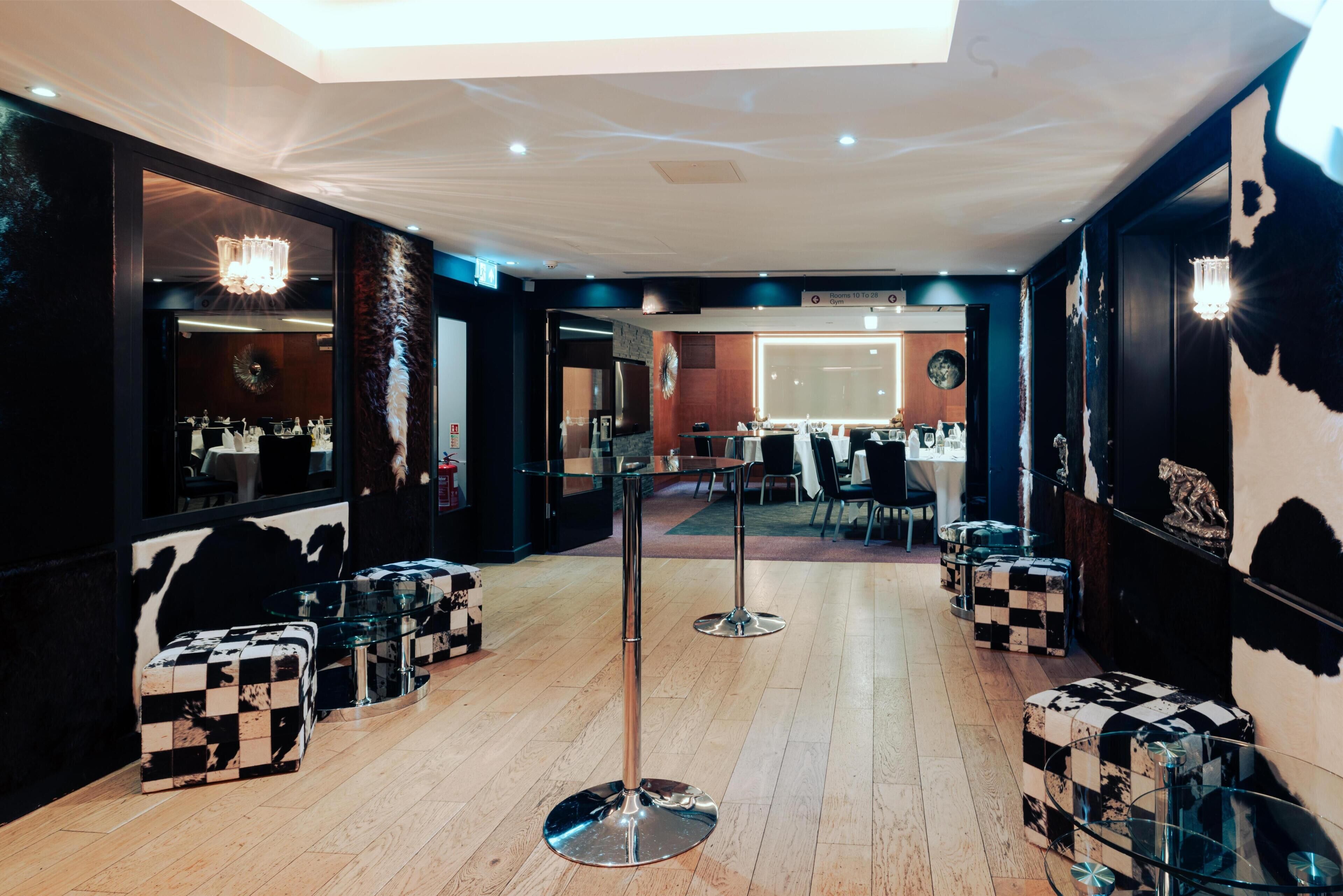 A hotel lobby with a high ceiling, a chandelier, checkered ottomans, and a reception desk.