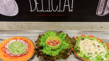 Tres platos de comida con lechuga, tomates y queso rallado, expuestos en una barra con un cartel que dice "DELICIA!"