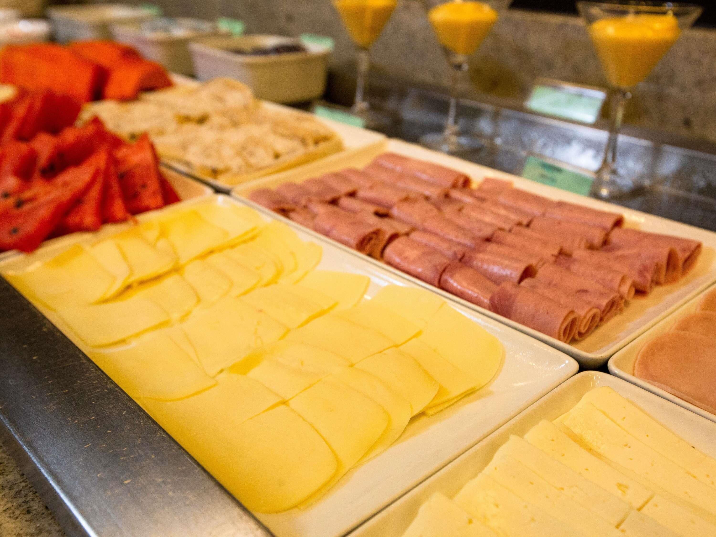 Un bufé con diversos alimentos, incluyendo queso en rodajas, jamón y fruta.
