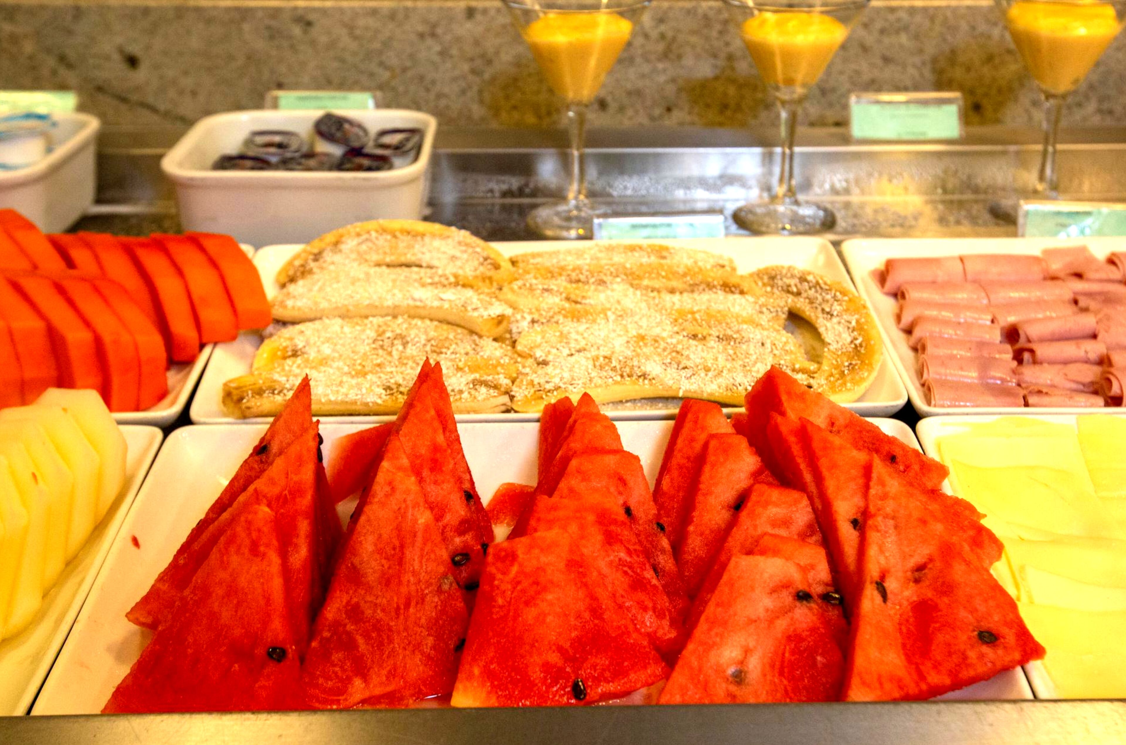 A buffet with various food items including sliced fruits, pastries, and meats.