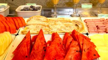 A buffet with various food items including sliced fruits, pastries, and meats.