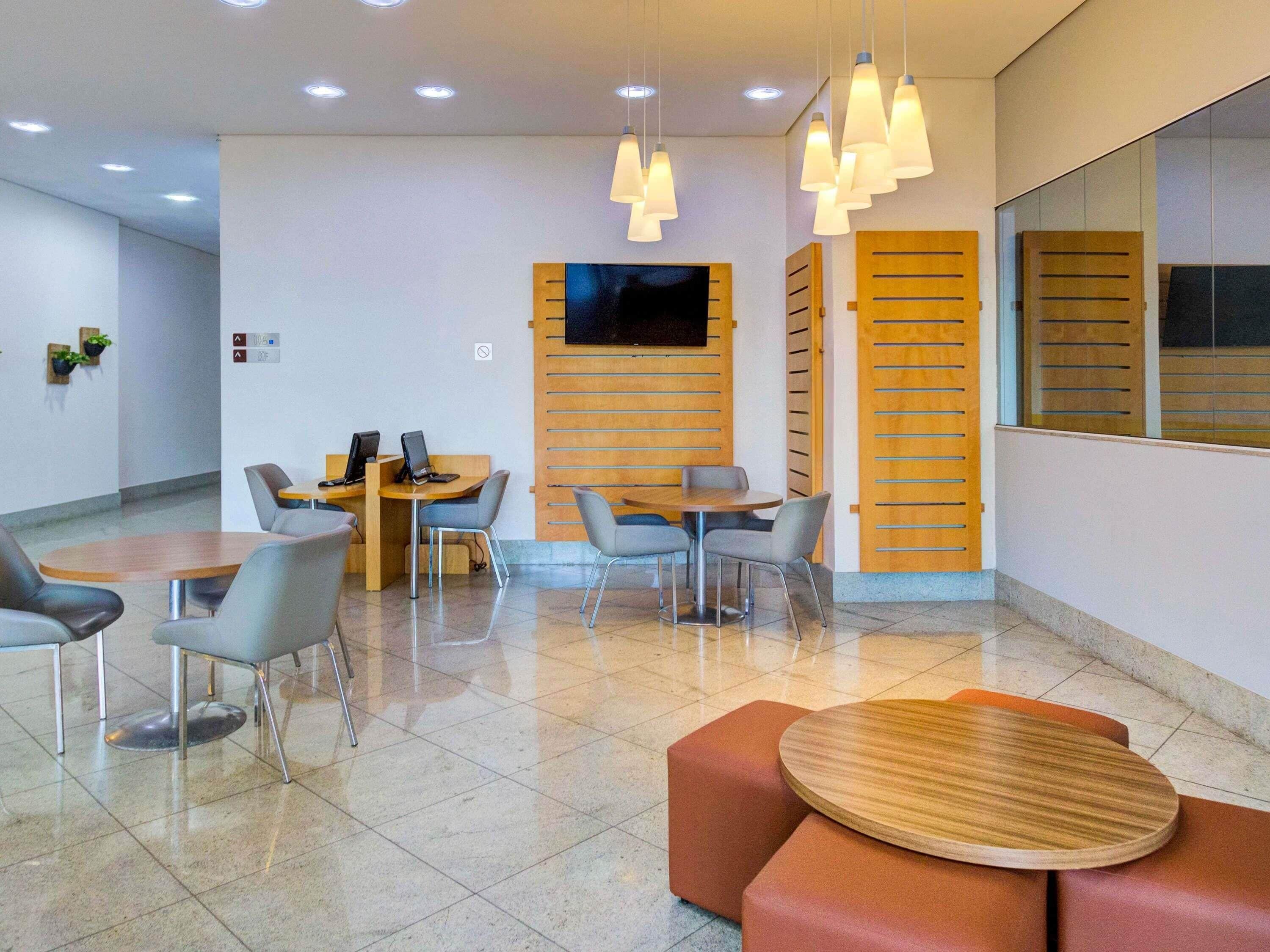 Un área de espera moderna con una mesa redonda, varias sillas, un sofá e iluminación colgante.