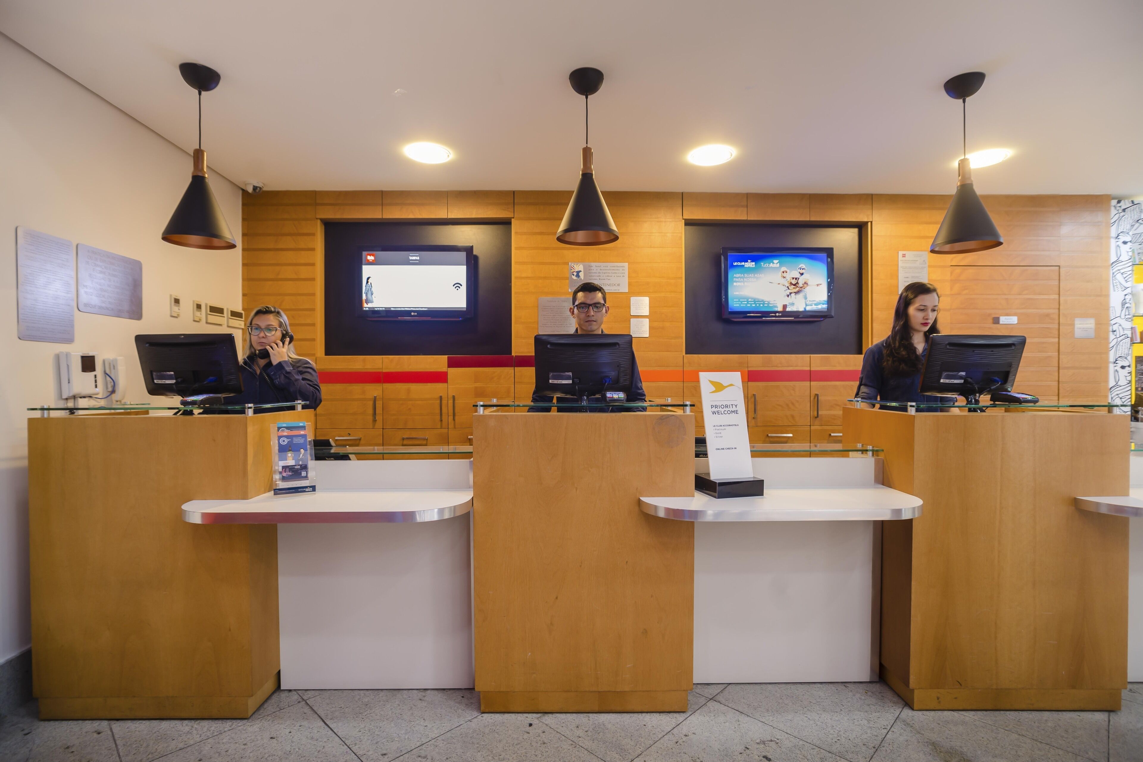 A reception area with three receptionists at their desks, wooden paneling, and two televisions on the wall.