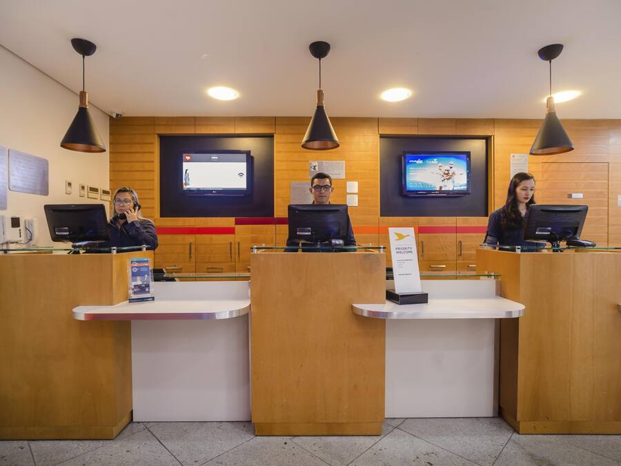 Ett receptionsområde med tre receptionspersonal vid sina diskar, träpanel på väggarna och två tv-apparater på väggen.