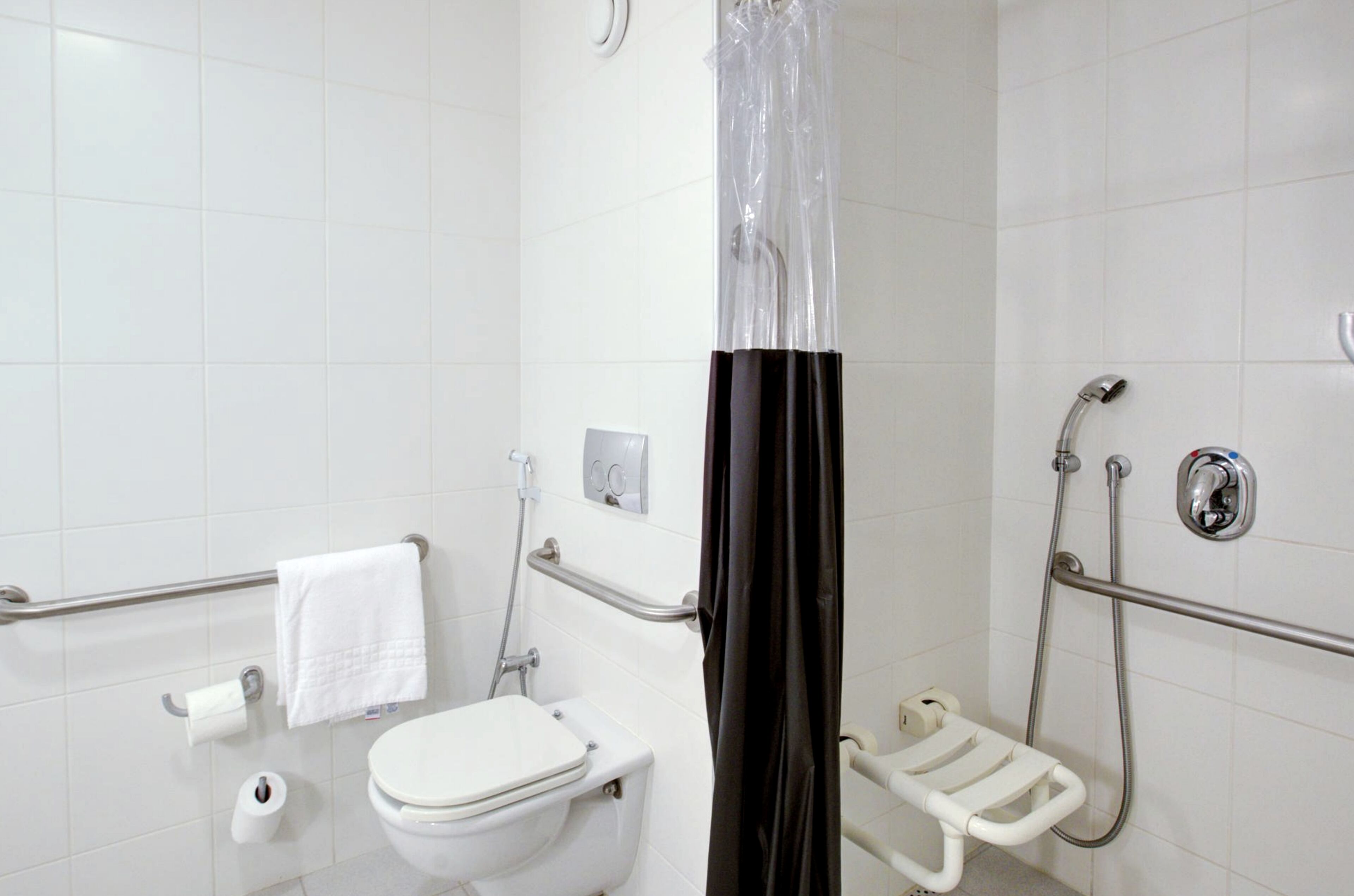 A bathroom with a white toilet, a shower with a grab bar, a white towel, and a roll of toilet paper.