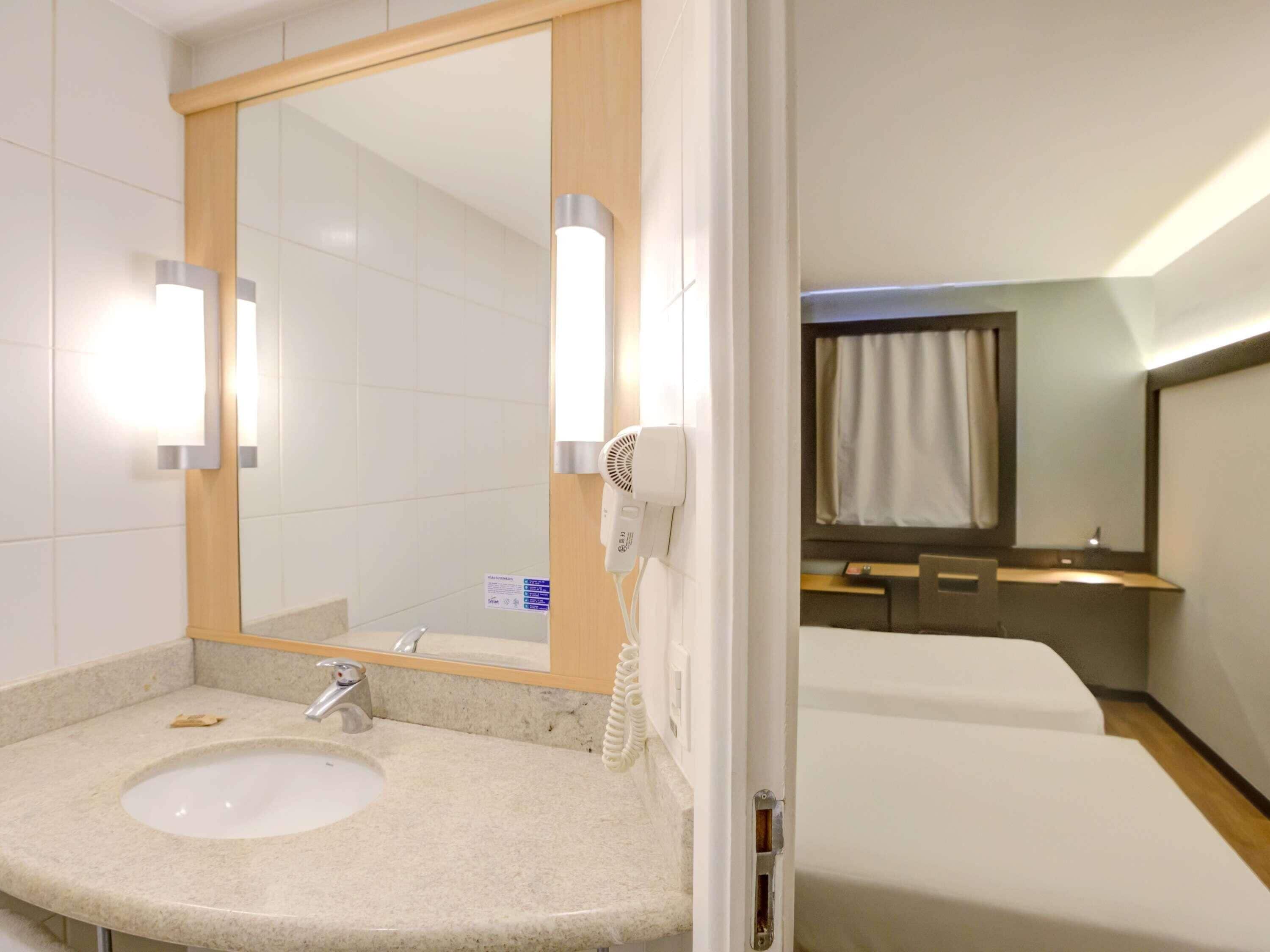 Un baño de hotel con lavamanos, espejo y secador de pelo.