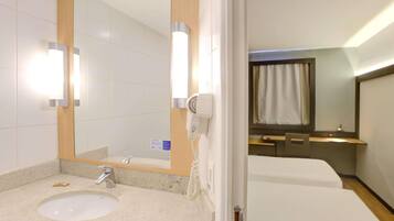 Un baño de hotel con lavamanos, espejo y secador de pelo.