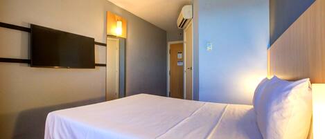Habitación de hotel con cama, televisor de pantalla plana en la pared y aire acondicionado.