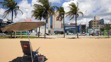 A beach with a chair and umbrella labeled 'ibis' and a building in the background.