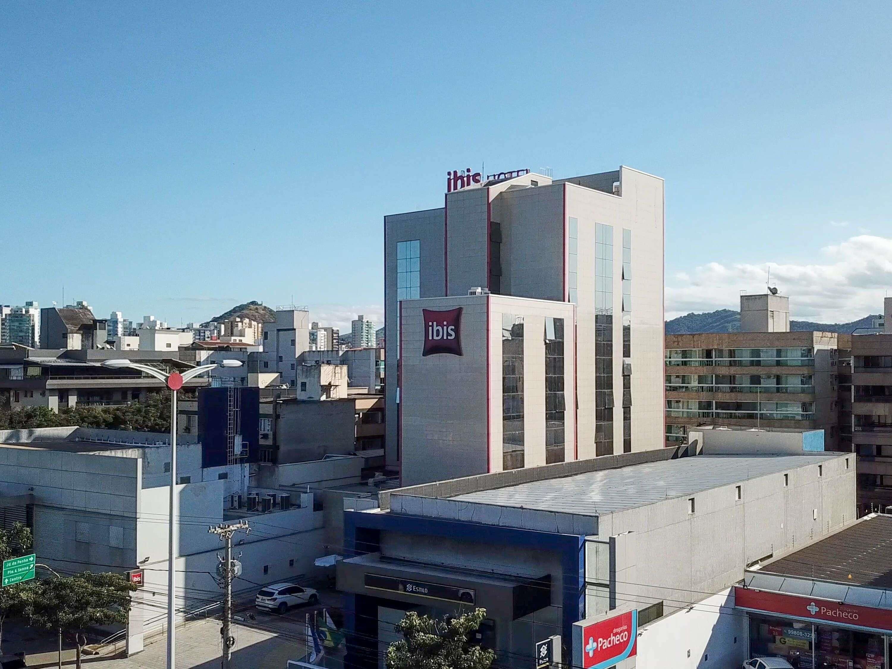 Een modern gebouw met een opvallend ‘ibis’ logo, omringd door andere gebouwen en een heldere lucht.